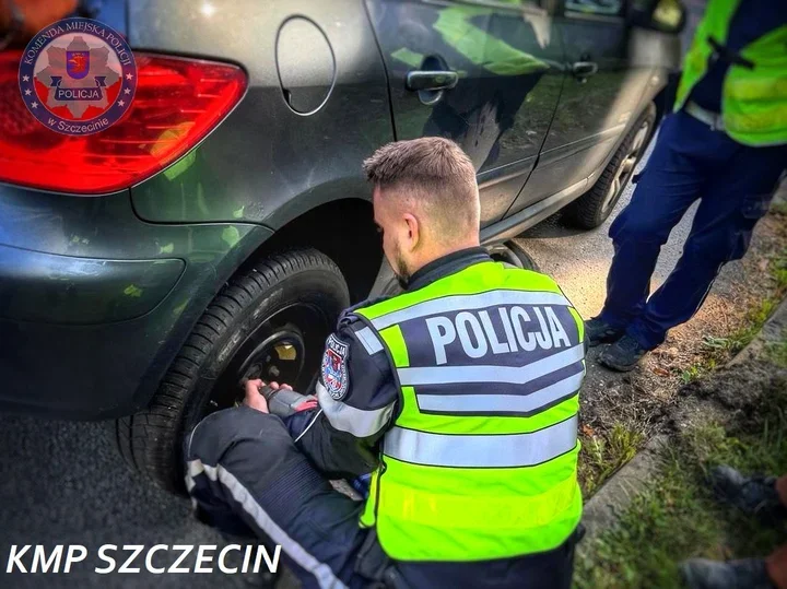 Policjant w kamizelce odblaskowej z napisem POLICJA wymienia koło w samochodzie osobowym na drodze.