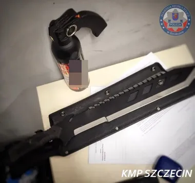 Zabezpieczone przez szczecińską policję przedmioty: gaz pieprzowy i duży nóż/macheta leżące na biurku obok dokumentów.