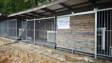 Nowoczesne drewniano-metalowe kojce dla zwierząt z tablicą informacyjną o konkursie „Nasze Zwierzaki 2026" stoją na terenie zielonym.