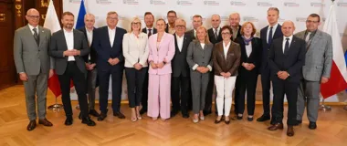 Grupa osób w eleganckim stroju biznesowym pozuje do pamiątkowego zdjęcia w pomieszczeniu reprezentacyjnym przed ścianką z logotypami Ministerstwa Edukacji Narod