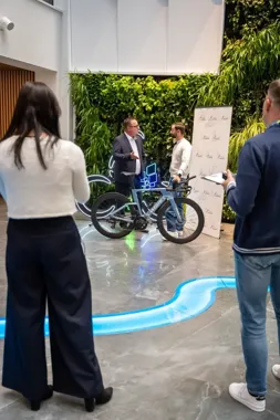Cztery osoby w nowoczesnym holu z zielną ścianą stoją wokół roweru szosowego marki S-Works, jeden mężczyzna gestykuluje podczas rozmowy.